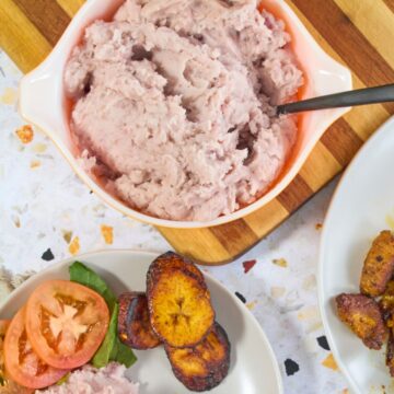 Puerto Rican mashed malanga in a vintage orange Pyrex dish served with fried sweet plantains and chuletas on white plates.