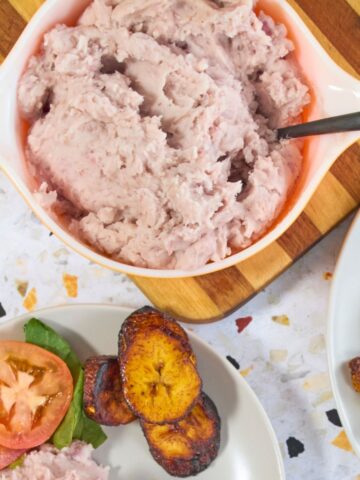 Puerto Rican mashed malanga in a vintage orange Pyrex dish served with fried sweet plantains and chuletas on white plates.