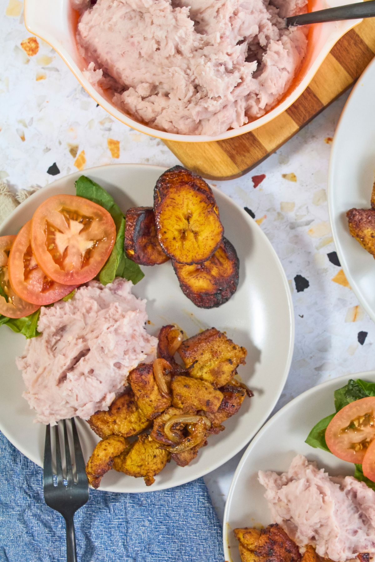 Overhead view of mashed malanga in a vintage orange Pyrex dish served alongside chuletas, maduros, lettuce, and tomato on white plates.
