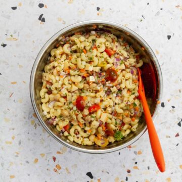 Completed pasta salad with elbow macaroni, chickpeas, diced vegetables, cherry tomatoes, and cheese cubes in a stainless steel bowl.