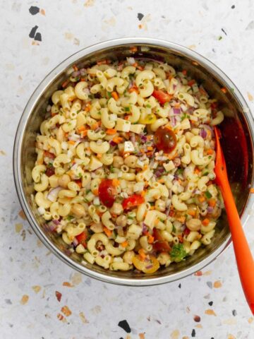 Completed pasta salad with elbow macaroni, chickpeas, diced vegetables, cherry tomatoes, and cheese cubes in a stainless steel bowl.