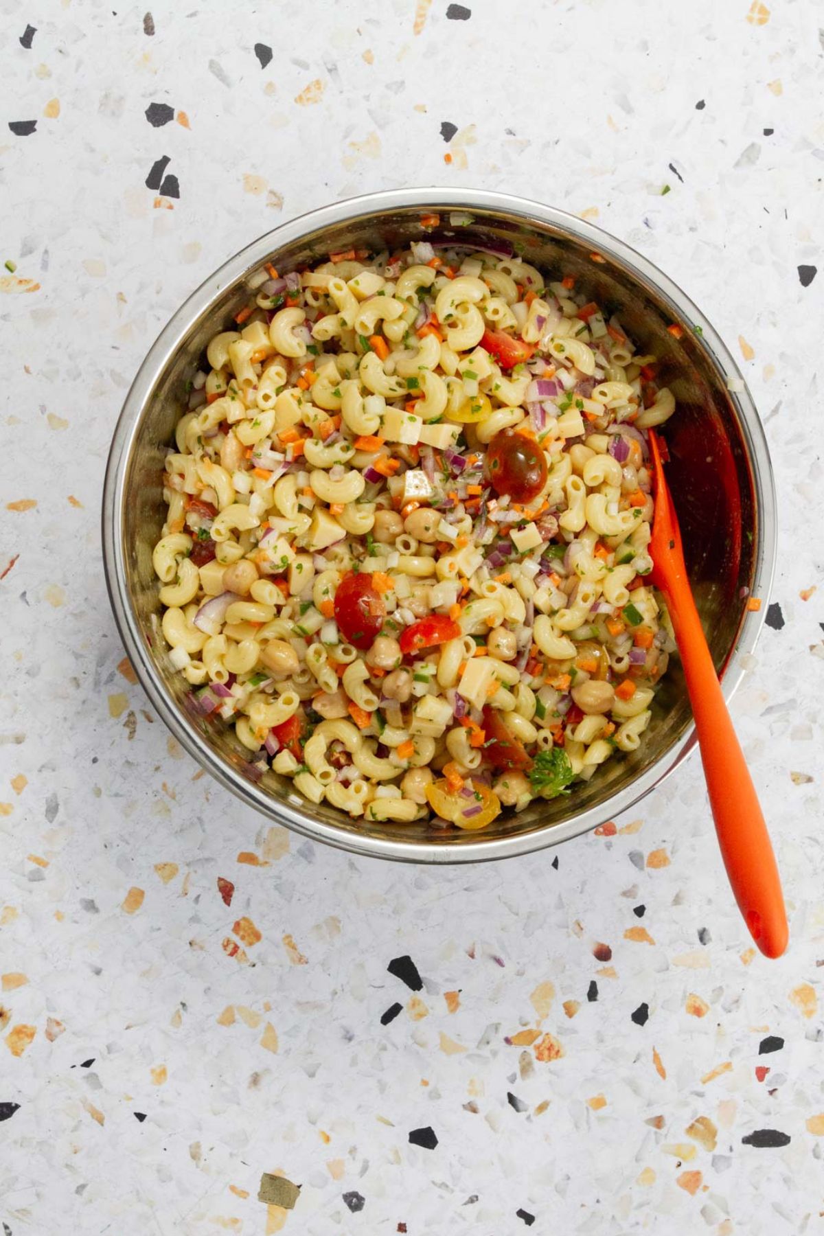 Fresh pasta salad with macaroni, chickpeas, colorful vegetables, and herbs ready to serve in a metal mixing bowl.
