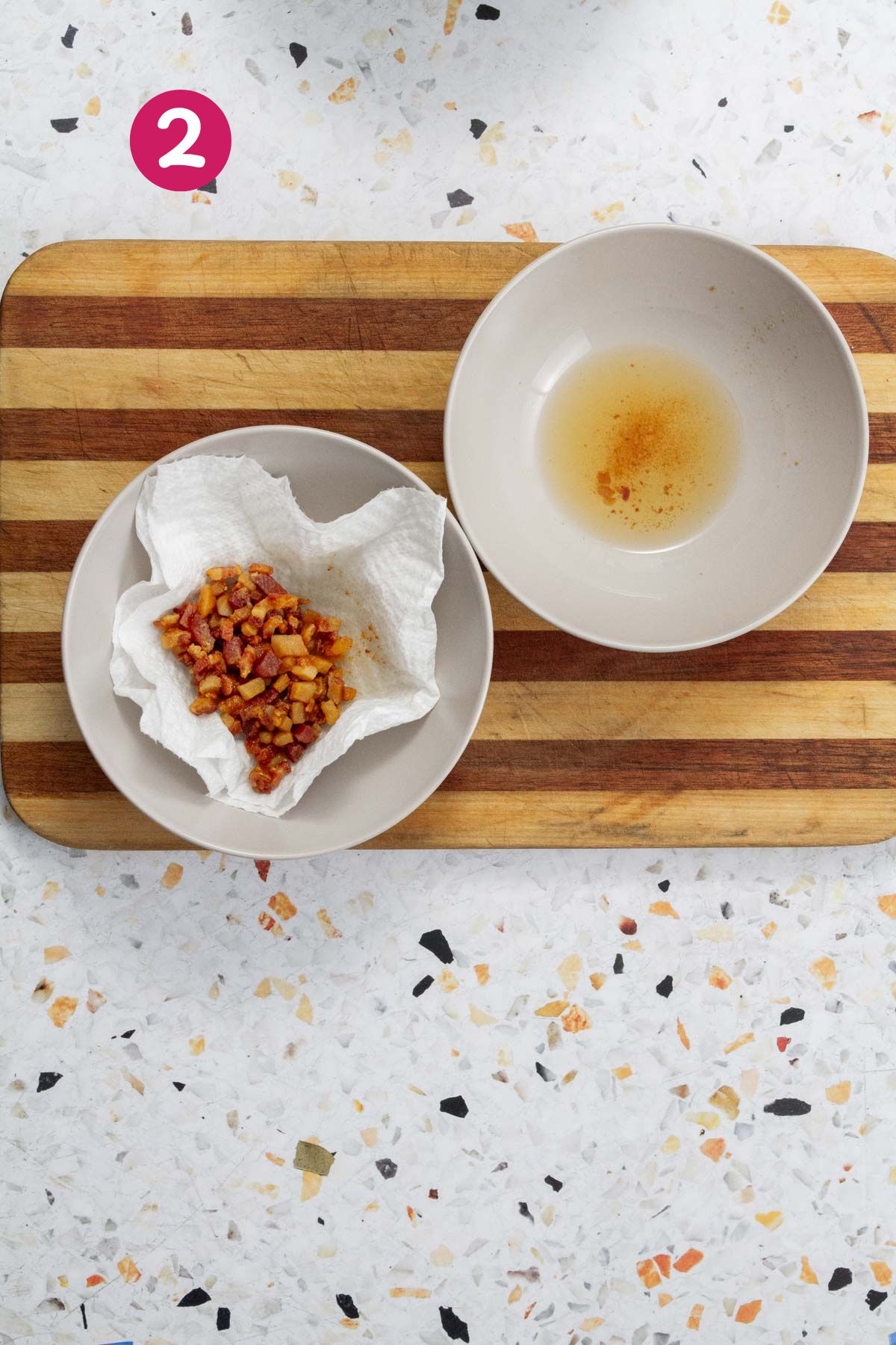 Crispy, rendered bacon pieces are draining on a paper towel, with the reserved bacon fat in a white bowl.