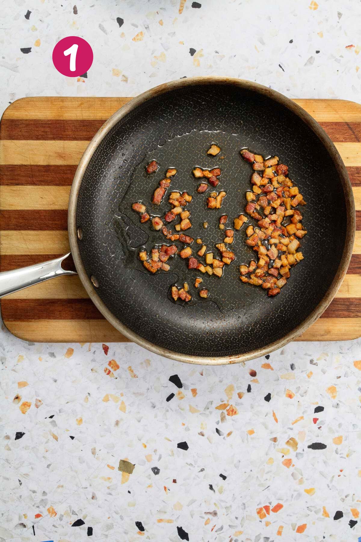Bacon pieces are cooking in a nonstick skillet until crispy and golden brown.