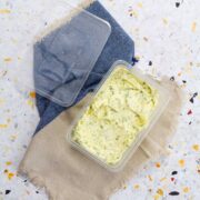 Roasted garlic and herb compound butter in an open clear storage container on a blue and tan linen.