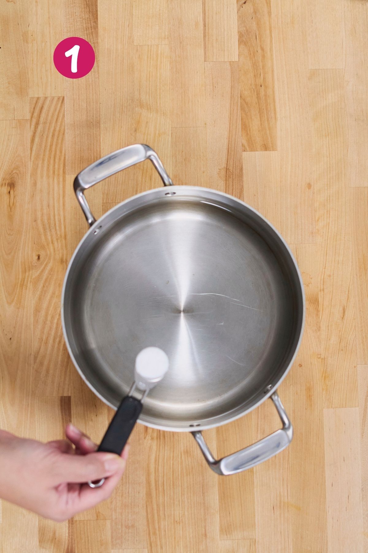(Step 1) Hand adding salt to an empty stainless steel pot before boiling plantains for pastelón.