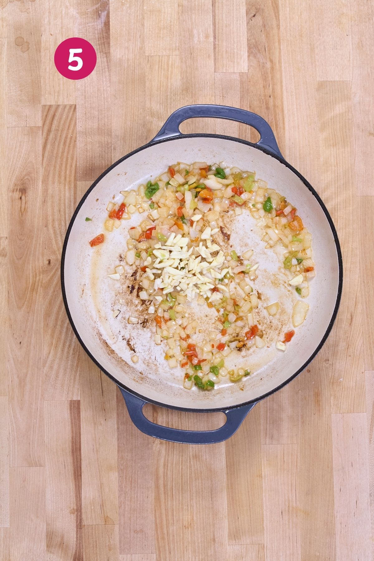 Sliced garlic added to sautéed onions and ají dulce in an enameled cast-iron pan.