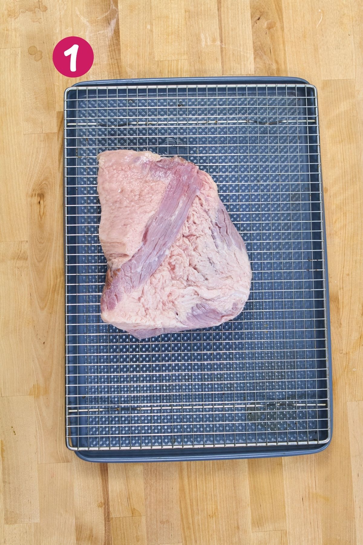 Raw corned beef brisket is draining on a wire rack over a baking sheet after being rinsed of the brining liquid.