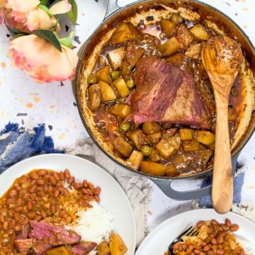 Puerto Rican corned beef brisket with potatoes and olives in a Dutch oven, served alongside plates of white rice and stewed beans.