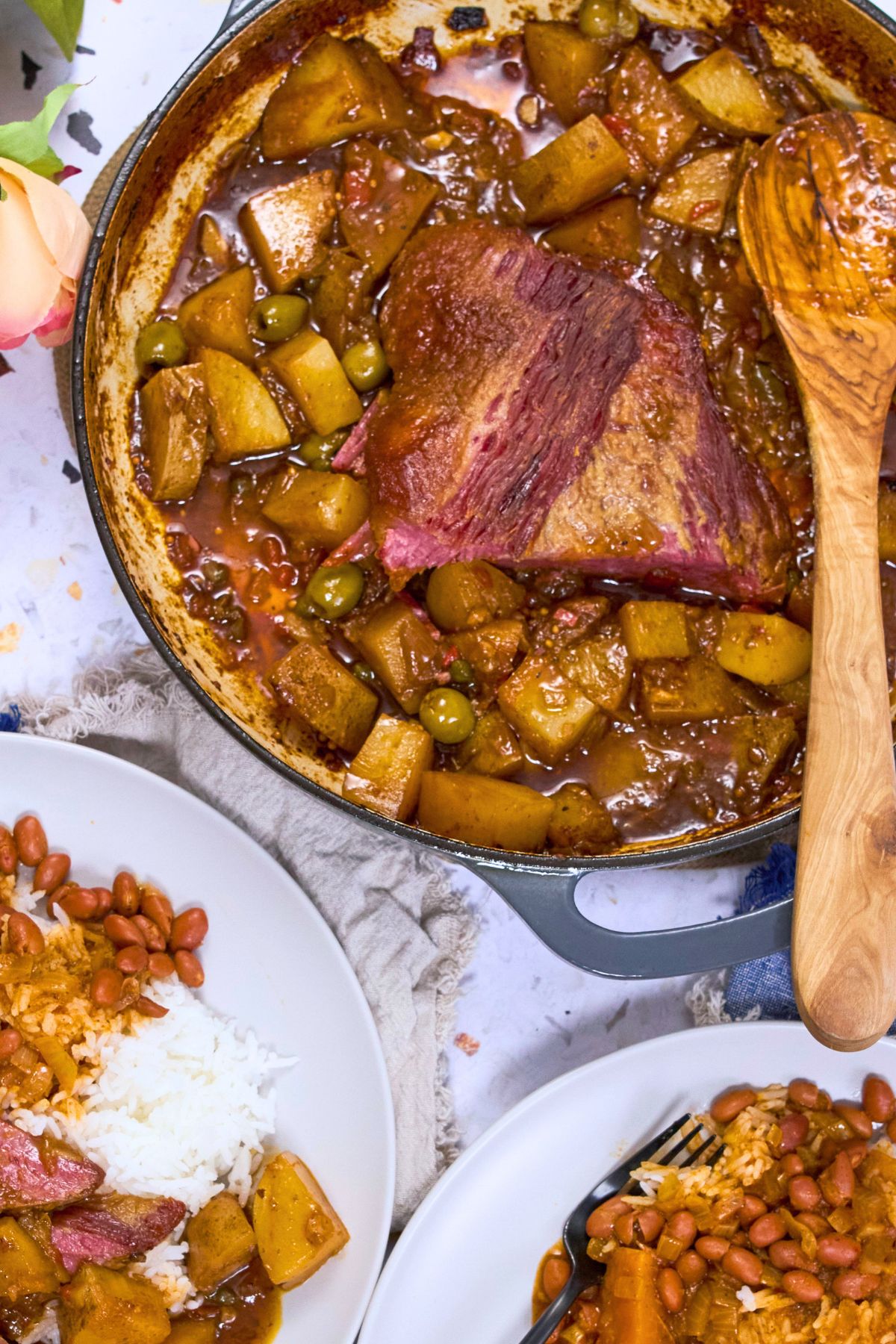 Close-up of Puerto Rican corned beef brisket in tomato-based sauce with golden potatoes and green olives in a Dutch oven.