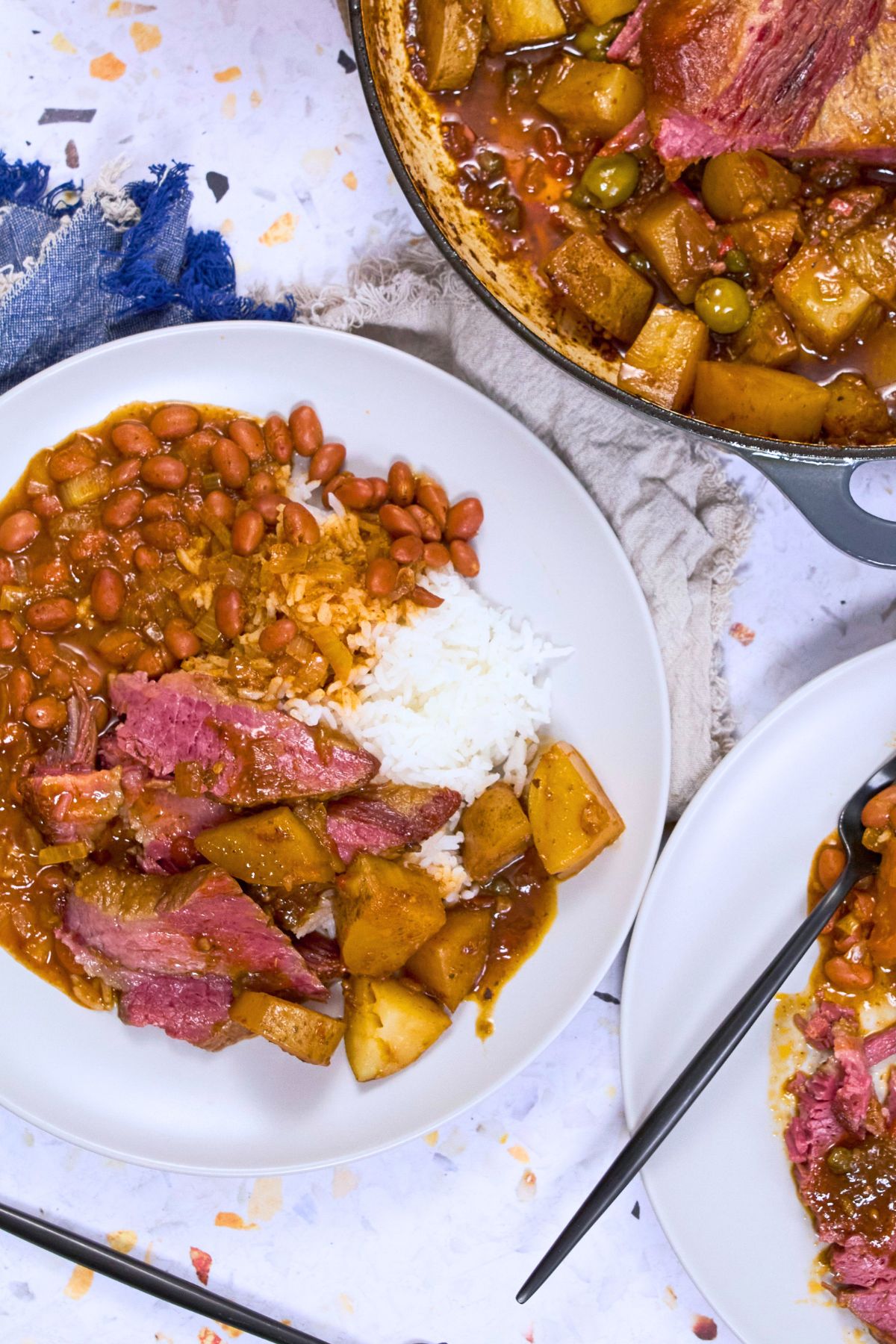 Sliced Puerto Rican corned beef with stewed potatoes over white rice and pink beans on a white plate.