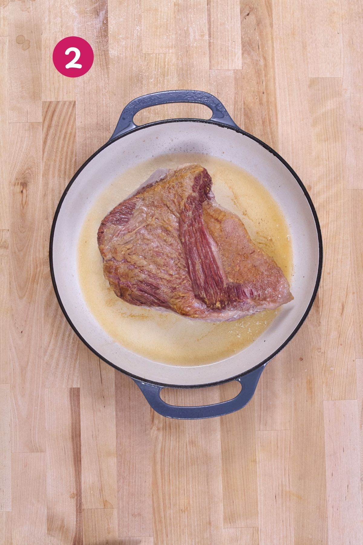 Corned beef brisket browning in rendered fat in an enameled cast-iron Dutch oven.
