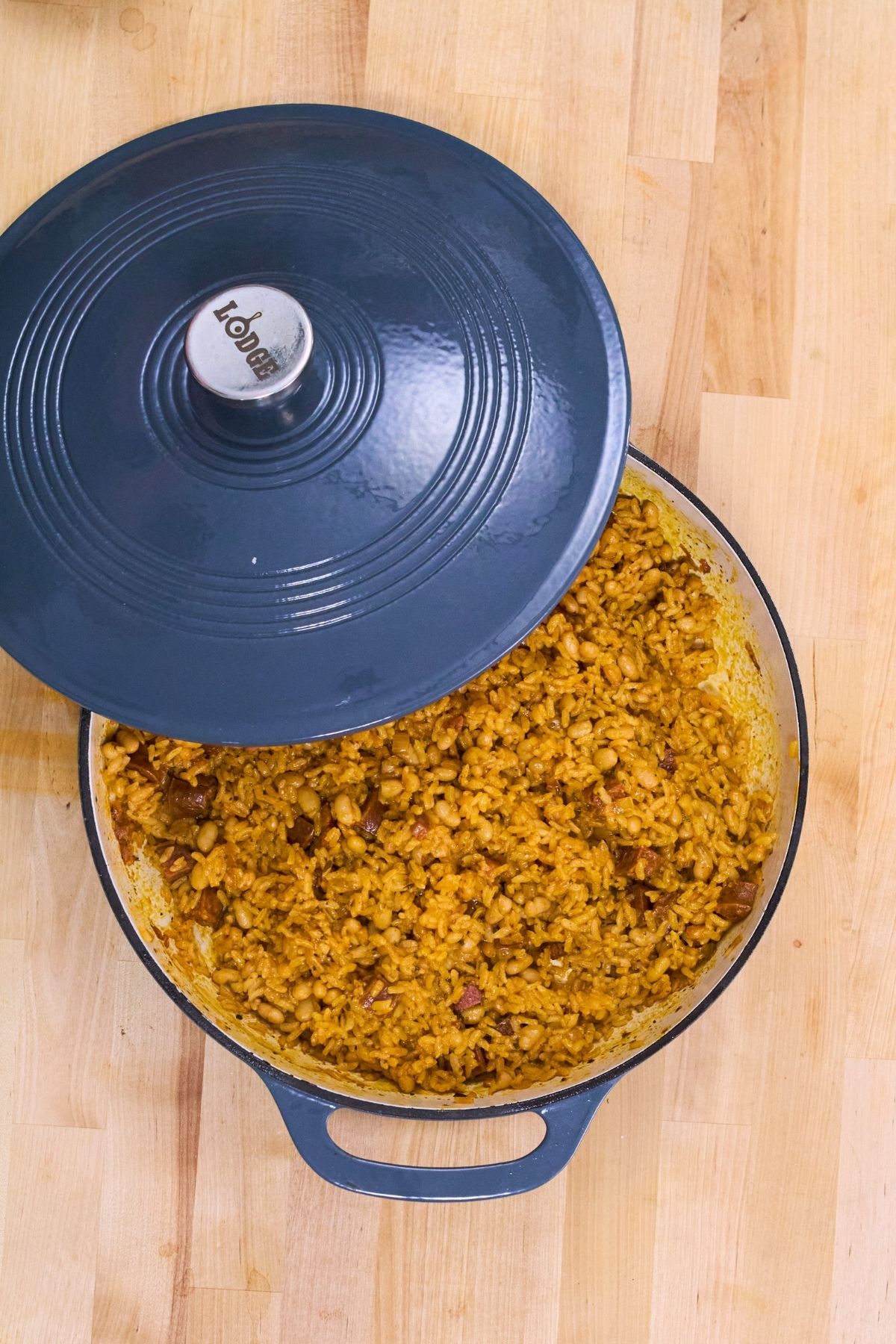 Overhead view of arroz con chorizo y habichuelas blancas in a Lodge Dutch oven with the lid lifted, showing the finished rice, white beans, and chorizo.