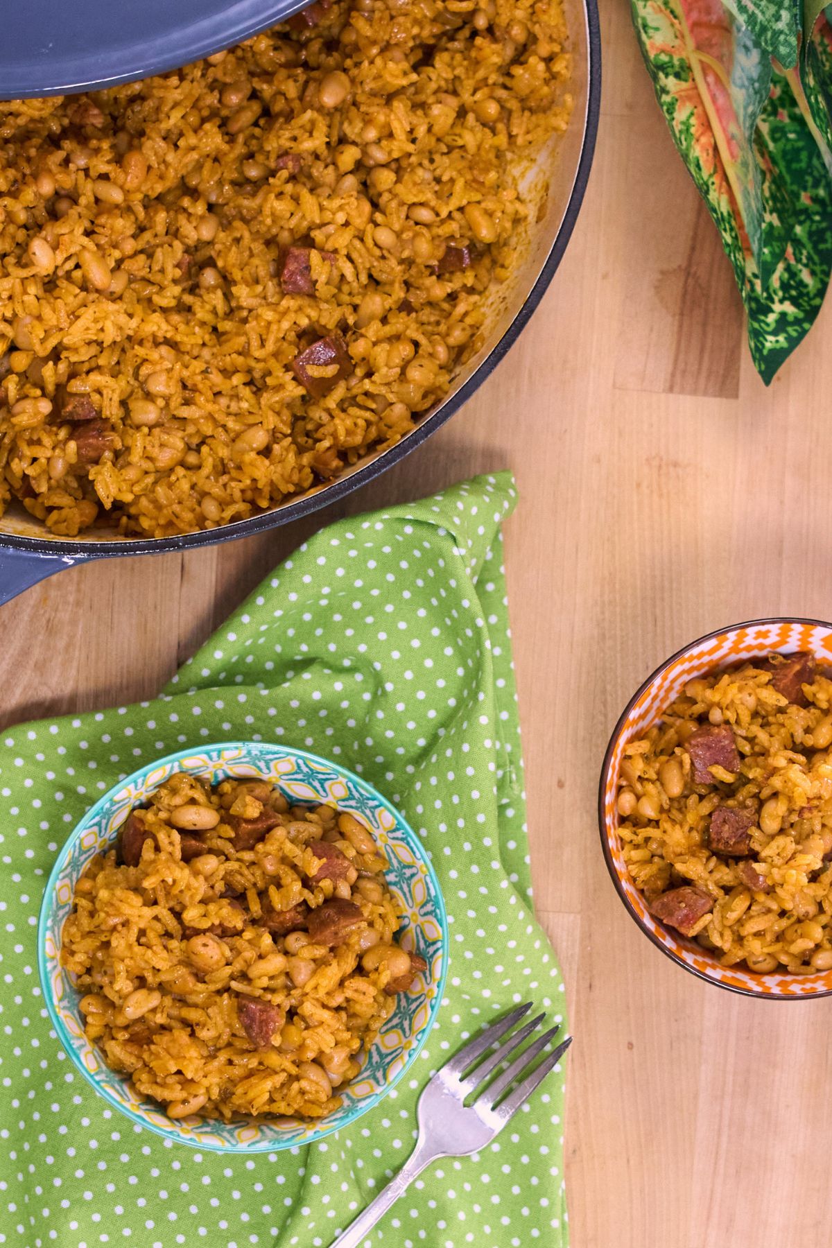 Close-up of two bowls of arroz con chorizo y habichuelas blancas garnished with forks, next to the Dutch oven and fresh flowers.