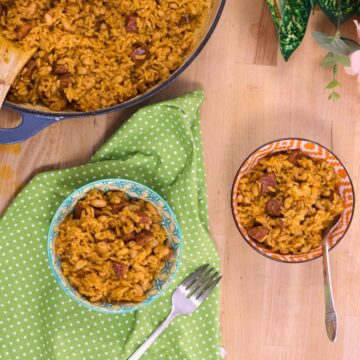 Two bowls of arroz con chorizo y habichuelas blancas served beside the Dutch oven, with forks and a green polka-dot napkin.