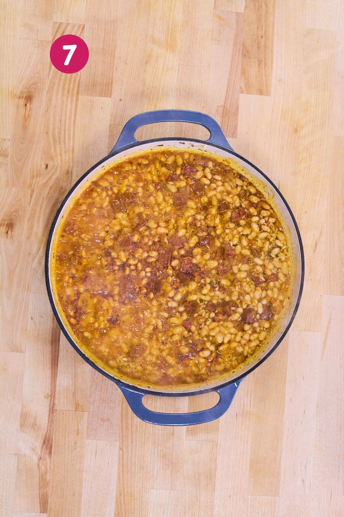 White beans, rice, and chorizo simmering in broth in a Dutch oven.